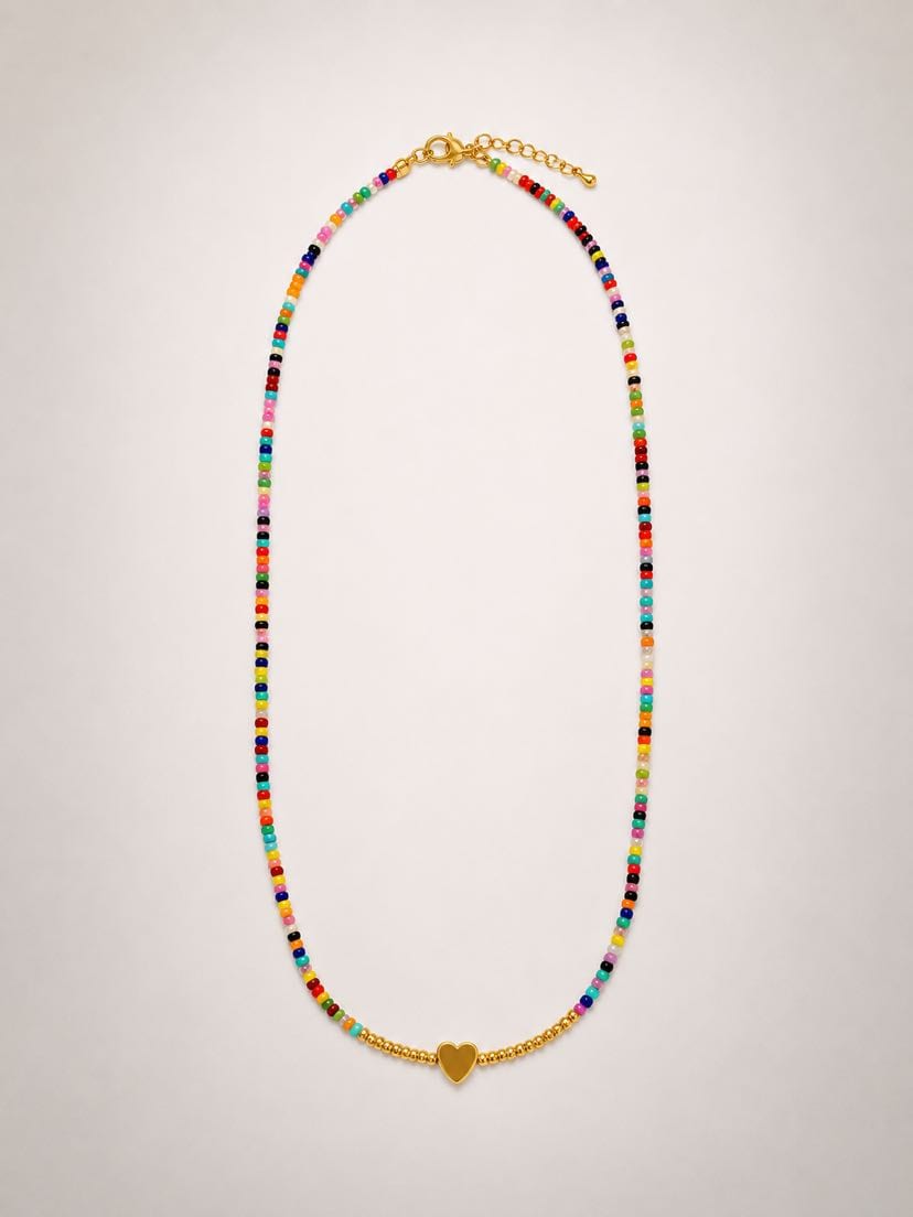 Collier Elena à plat sur fond crème, fil de perles de rocaille multicolores enfilées (rose, rouge, bleu, vert, turquoise, jaune, orange, noir, blanc), petit cœur d'or au centre encadré de six perles dorées rondes