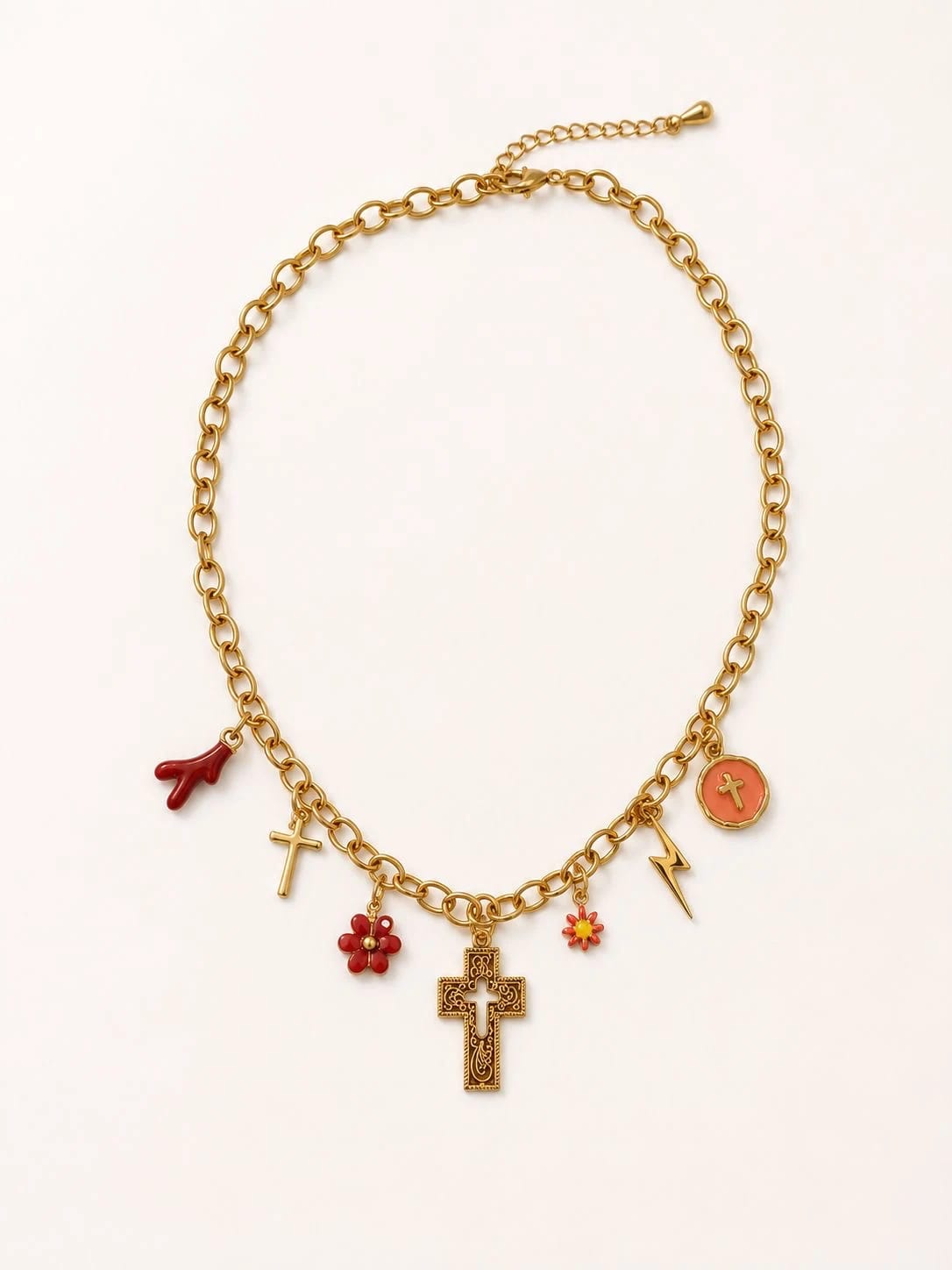 Packshot collier Corallia à plat sur fond crème, chaîne forçat d'or et 7 talismans rouges et or visibles — brin de corail rouge, petite croix dorée ciselée, fleur en émail rouge, crucifix byzantin central ciselé, fleur en émail rouge-orange, éclair d'or, médaillon rond émaillé orange, fermoir mousqueton et chaînette de rallonge en haut